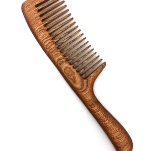 May include: A brown wooden comb with a curved handle. The comb has fine teeth and is made of natural wood.