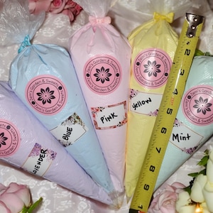 May include: Five piping bags filled with different colored frosting, labeled with the flavors lavender, blue, pink, yellow, and mint. The bags are arranged in a semi-circle with a measuring tape in the center.