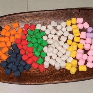 May include: A wooden oval dish filled with colorful, cylindrical candies. The candies are arranged in sections of black, orange, red, green, white, yellow, pink, and purple. The dish is made of dark wood.
