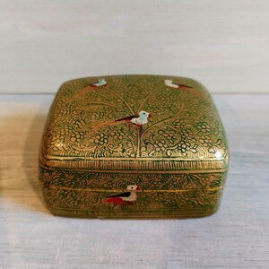 May include: A square, green decorative box with gold trim and a floral design. The box features small birds with red, white, and black details. The box is likely used for storing small items.