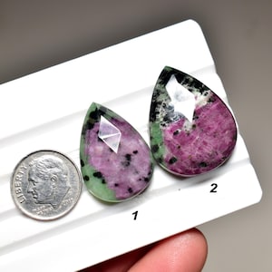 May include: Two faceted, teardrop-shaped gemstones with a mix of colors. The gems feature a vibrant pinkish-red hue with black and green inclusions. A dime is included for size comparison. The gems are numbered 1 and 2.