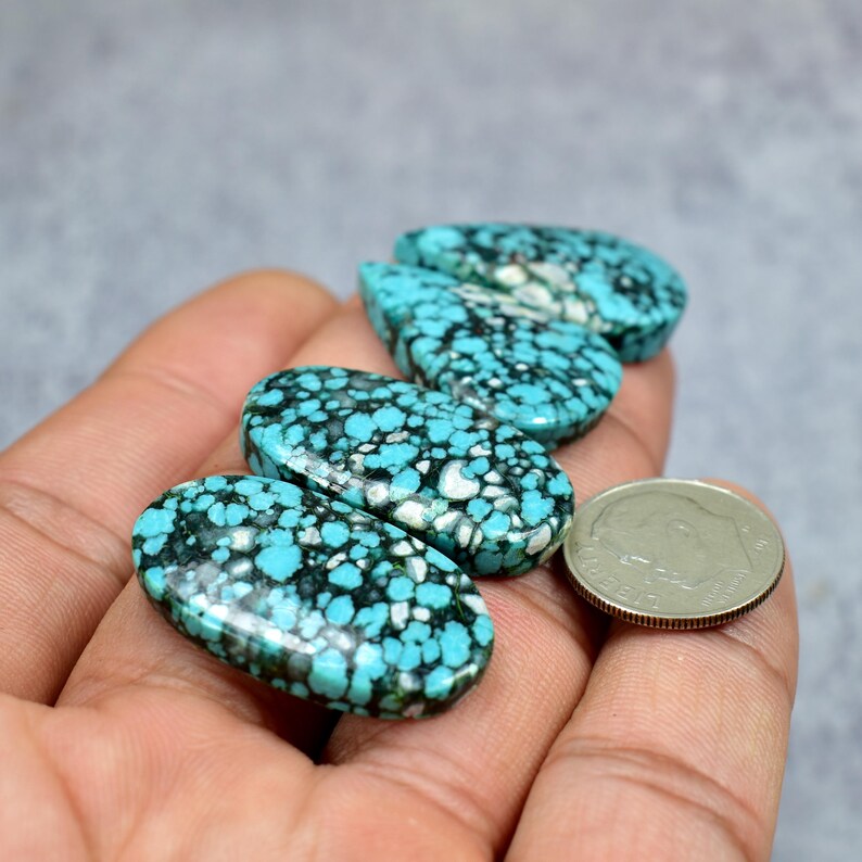 Puede incluir: Cuatro piedras preciosas ovaladas de turquesa con un patr&oacute;n moteado de azul y negro, exhibidas en una mano. Una moneda de plata est&aacute; al lado de las piedras para comparar el tama&ntilde;o. Las piedras preciosas tienen una superficie pulida y lisa.