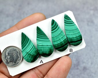 May include: Four teardrop-shaped malachite cabochons with distinct green banded patterns arranged on a white card. A US dime is placed next to the stones for scale, with the letters A and B printed below two of the malachite pieces.