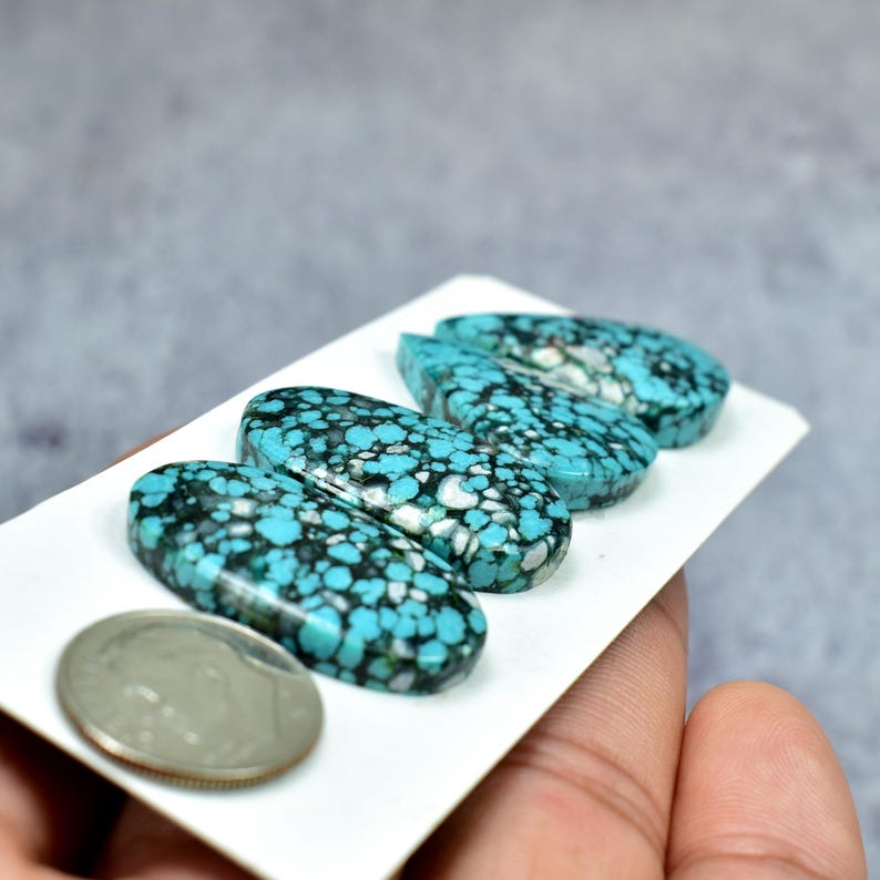 Puede incluir: Cuatro piedras preciosas ovaladas de turquesa con patrones de matriz negros y blancos. Las piedras se muestran en una tarjeta blanca, con una moneda de plata para comparar el tama&ntilde;o. Superficie pulida.