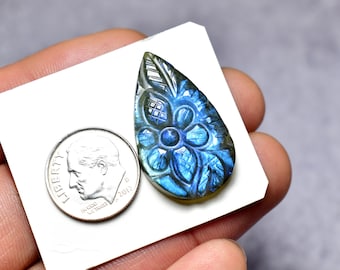 May include: A carved labradorite gemstone pendant with a floral design. The pendant is teardrop-shaped and features a detailed carving of a flower and leaves. The gemstone has blue and green iridescent colors. A U.S. dime is next to the pendant for size comparison.