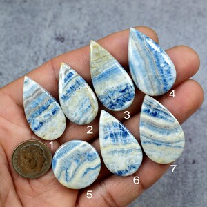 May include: Seven polished gemstones in various shapes, including teardrop and round, with a mix of blue, white, and tan colors. A U.S. dime is included for size comparison. The stones have a marbled appearance, suggesting they are a type of mineral.