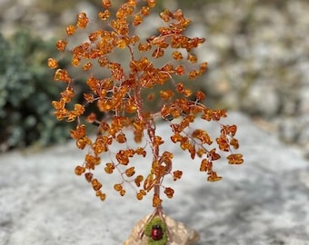 May include: A small amber tree sculpture with a red ladybug at the base. The tree is made of wire and amber beads and is sitting on a small rock base.
