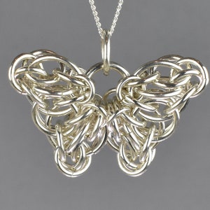 May include: A silver butterfly pendant necklace made of intricate woven metal links. The pendant is detailed and delicate, with a smooth, polished finish.