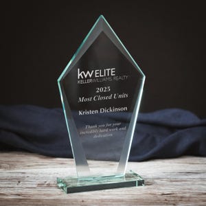 May include: A clear glass award in the shape of a diamond with the text "kw ELITE KELLERWILLIAMS REALTY 2025 Most Closed Units Kristen Dickinson Thank you for your incredibly hard work and dedication" engraved on it.