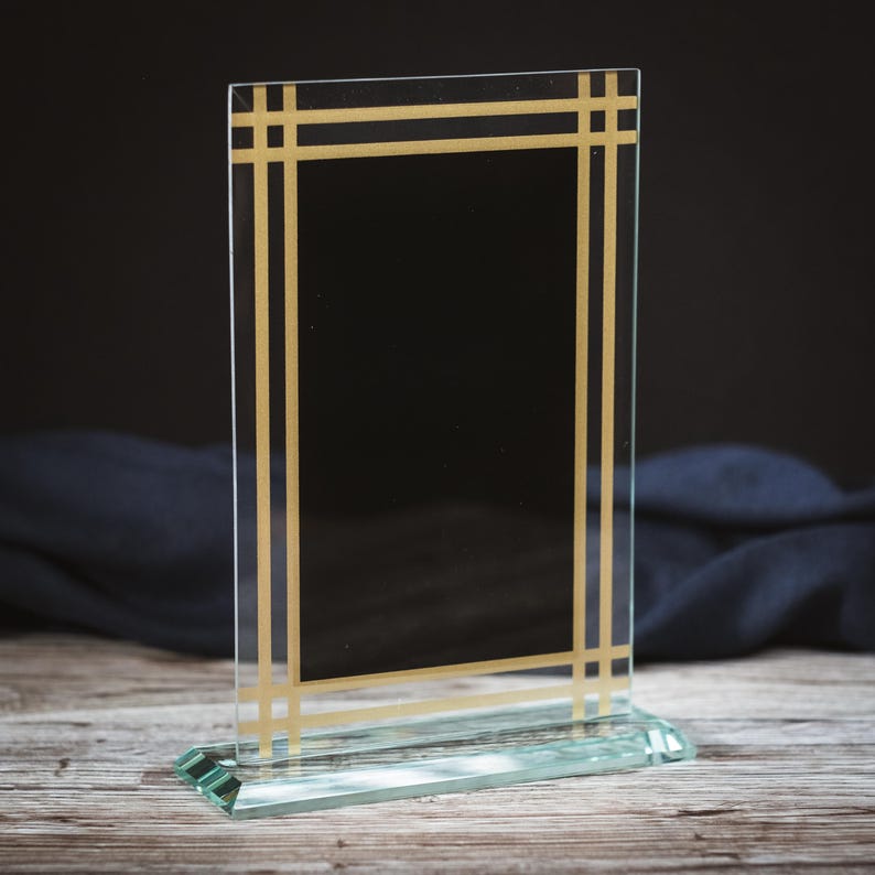 May include: A clear glass award plaque with a gold frame. The plaque has a black background and is ideal for engraving.