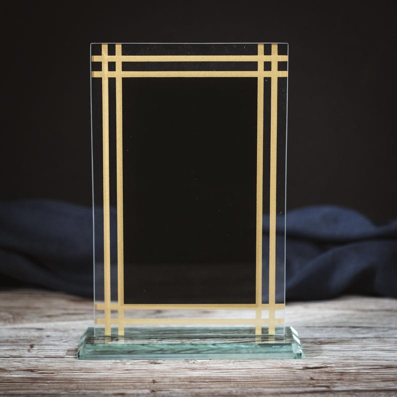 May include: A clear glass award plaque with a gold border. The plaque has a rectangular shape and a flat base.