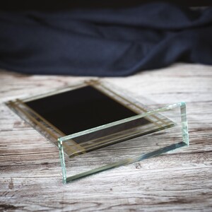 May include: A glass plaque with a gold border and a black background. The plaque is lying on a wooden surface.