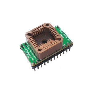 May include: A green circuit board with a brown plastic DIP24 socket for an integrated circuit. The board has the text "PLCC28T-DIP24 0.6" printed on it.