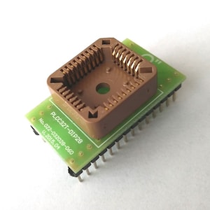 May include: A brown plastic DIP28 socket on a green circuit board with gold-plated pins. The board has the text "PLCC32T-DIP28" and "No. 022-032028-060 U-2015.04" printed on it.