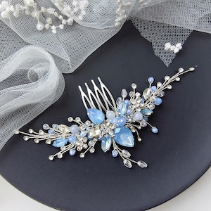 May include: A silver hair comb featuring light blue teardrop crystals, clear rhinestones, and small white beads arranged in a floral spray pattern, accompanied by a piece of white tulle fabric adorned with scattered white pearls.
