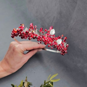 以下が含まれることがあります： 赤いビーズと銀の葉が付いた銀色のヘッドバンド。ヘッドバンドは、小さな赤い丸いビーズと銀の葉で飾られています。