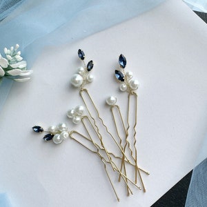 May include: A set of four gold-toned metal hair pins featuring decorative clusters of white faux pearls and dark blue marquise-cut crystals. Each pin has a wavy U-shaped base, with the embellishments wired onto the top of the metal prongs.