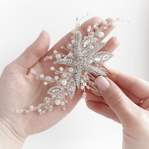 Può includere: Pettine per capelli argentato con un design a stella marina, decorato con strass e perle.