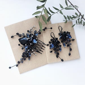 May include: A hair comb and a pair of matching earrings featuring dark blue and black crystals, beads, and clear rhinestones arranged on thin black wire branches. The hair comb has a multi-pronged base, and the earrings have hook-style backings.