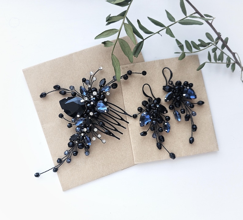 May include: A hair comb and a pair of matching earrings featuring dark blue and black crystals, beads, and clear rhinestones arranged on thin black wire branches. The hair comb has a multi-pronged base, and the earrings have hook-style backings.
