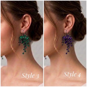 May include: Two dangling earrings featuring clusters of faceted crystals. The left earring, labeled Style 3, has emerald green crystals. The right earring, labeled Style 4, has deep purple crystals. Both earrings are set in dark metal with a hook closure.