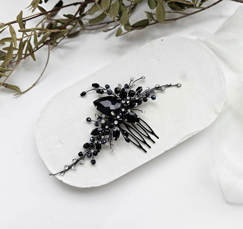 May include: A hair comb featuring a black metal base adorned with clusters of faceted black crystals, dark beads, and small clear rhinestones arranged on thin, flexible wire branches that extend outward from the central decorative element.