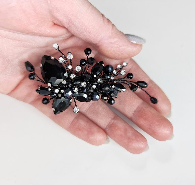 May include: A decorative hair accessory featuring a cluster of black teardrop-shaped crystals, small round black beads, and clear sparkling rhinestones set on thin, flexible black wire branches that extend outward in a spray pattern.
