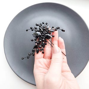 May include: A black hair pin featuring a cluster of faceted black beads and crystals arranged on thin, flexible black wire branches. The decorative element is shaped like a floral spray with various bead sizes and shapes, attached to a two-pronged pin.