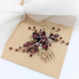 May include: A hair comb featuring a gold-tone metal base adorned with deep burgundy teardrop crystals, small round burgundy beads, and clear sparkling rhinestones arranged in a floral-inspired spray pattern on thin, flexible gold-colored wire branches.