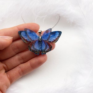 Hand holds blue butterfly pendant necklace on white feathers background