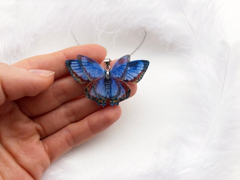 Hand holds blue butterfly pendant necklace on white feathers background