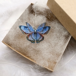 Blue butterfly pendant necklace in a gift box on white feathers background