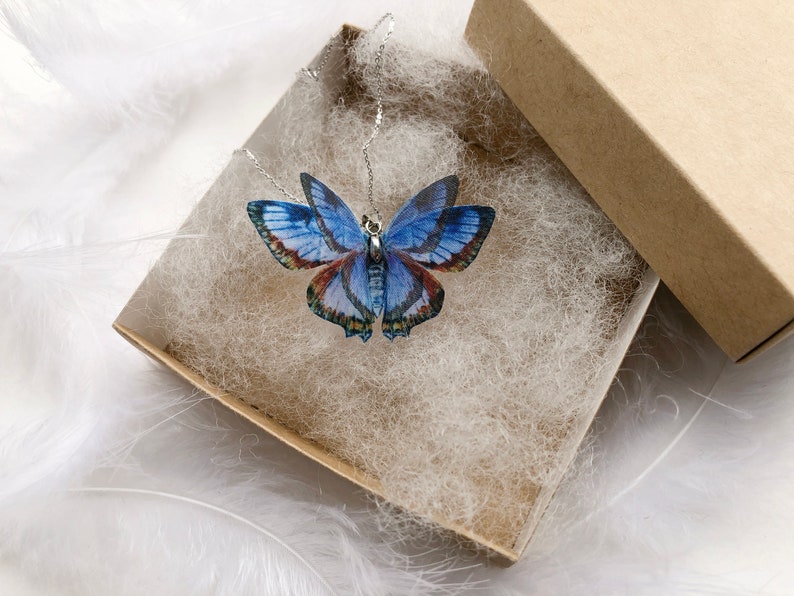 Blue butterfly pendant necklace in a gift box on white feathers background