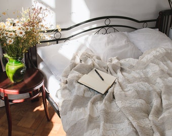 Könnte beinhalten: Ein weißes Bett mit einem schwarzen Metallrahmen und einer weißen und beigefarbenen Decke. Ein Notizbuch und ein Stift liegen auf der Decke. Ein Strauß weißer Blumen in einer grünen Vase steht auf einem Holztisch neben dem Bett.