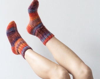 May include: A pair of colorful striped socks in shades of orange, red, and blue. The socks are worn on a person's legs, which are raised in the air.