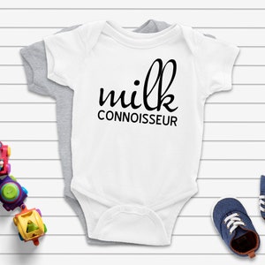 May include: White baby onesie with black text that reads "milk connoisseur".