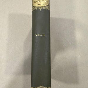 May include: A dark green hardcover book spine titled The French Revolution by Carlyle, Vol. II. The spine features gold embossed lettering and decorative filigree patterns at the top and bottom, with the publisher A.L. Burt New York at the base.