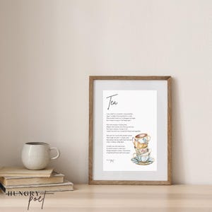 Op de afbeelding: Een ingelijste print met het woord "Tea" in script. De print toont een stapel aquarel theekopjes en een gedicht. Een keramische mok en een stapel boeken staan op een houten oppervlak.