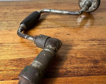 Op de afbeelding: Vintage handkrukboor met een zwarte houten handgreep en een metalen behuizing. De boor is aan de zijkant gemarkeerd met "WILCOX".