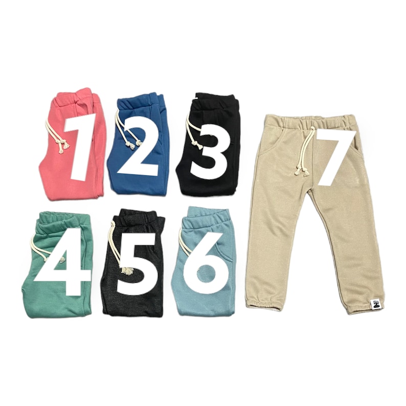 May include: A collection of seven pairs of sweatpants in various colors, including coral, blue, black, teal, charcoal, light blue, and tan. Each pair features a drawstring waist and a large white number. The sweatpants are displayed on a white background.