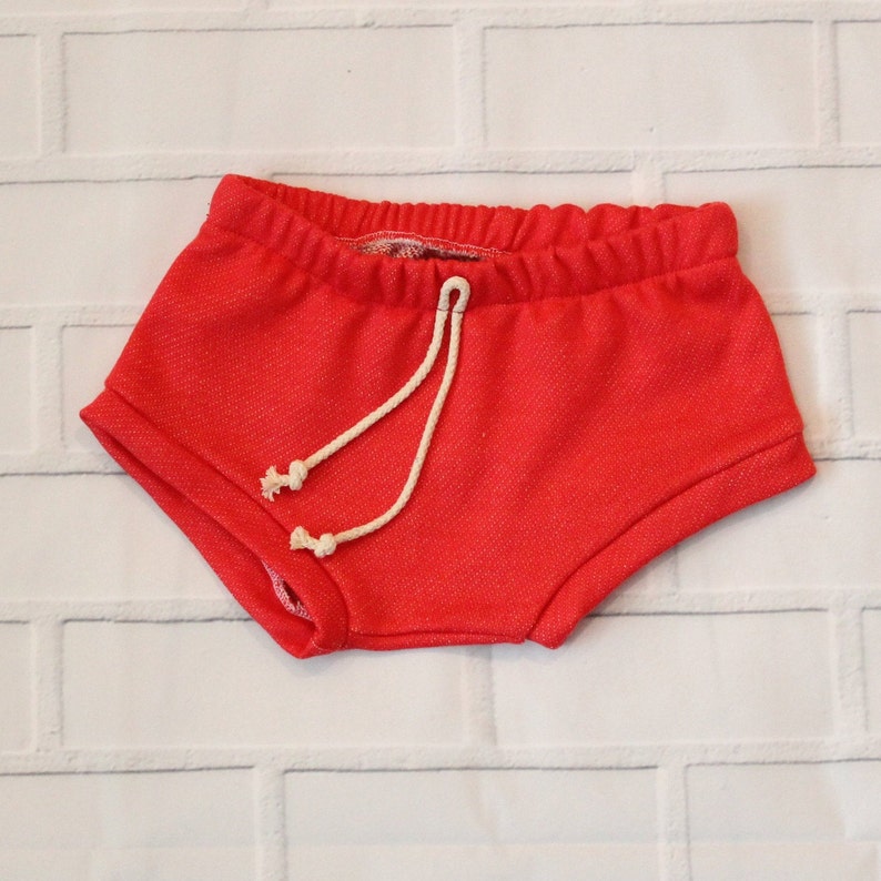 May include: Red shorts with a white drawstring. The shorts are made of a soft, textured fabric.