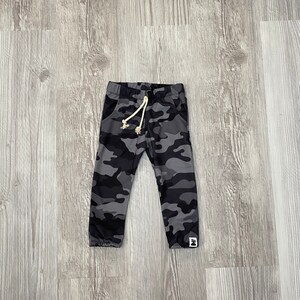 May include: Gray camouflage print sweatpants with a white drawstring and a small black and white logo on the right leg.