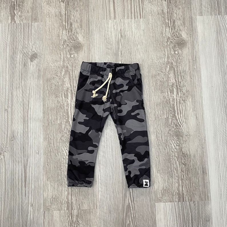 May include: Gray camouflage print sweatpants with a white drawstring and a small black and white logo on the right leg.