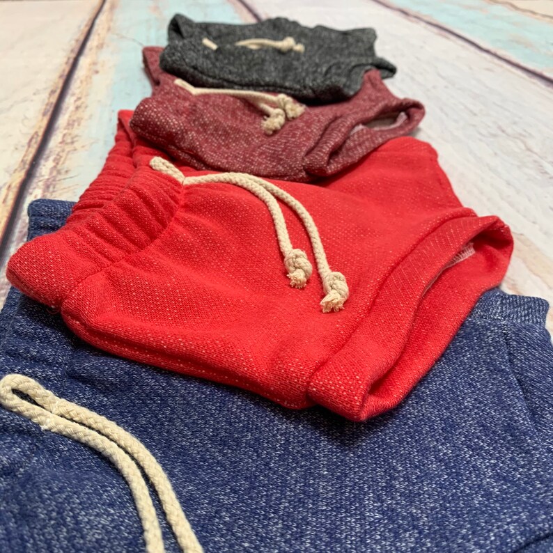 May include: Four pairs of drawstring shorts in different colors: navy blue, red, burgundy, and gray. The shorts are made of a soft, textured fabric.
