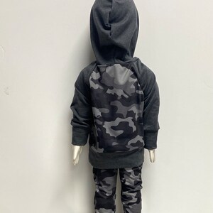 May include: A gray hooded sweatshirt with a camouflage pattern on the back and matching camouflage pants.