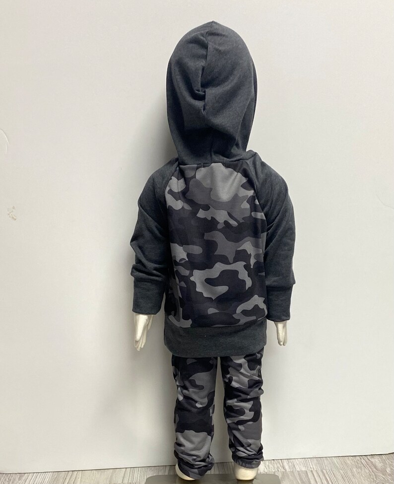 May include: A gray hooded sweatshirt with a camouflage pattern on the back and matching camouflage pants.