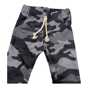 May include: Gray camouflage sweatpants with a white drawstring. The sweatpants have two pockets on the front.