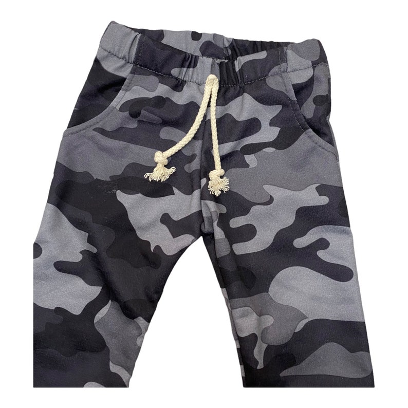 May include: Gray camouflage sweatpants with a white drawstring. The sweatpants have two pockets on the front.