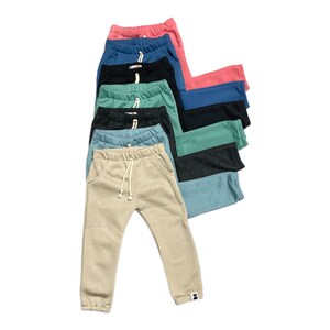 May include: A stack of colorful sweatpants in various shades, including pink, blue, black, and green. Each pair features a drawstring waist and pockets. The pants are made of a soft material and are suitable for casual wear.