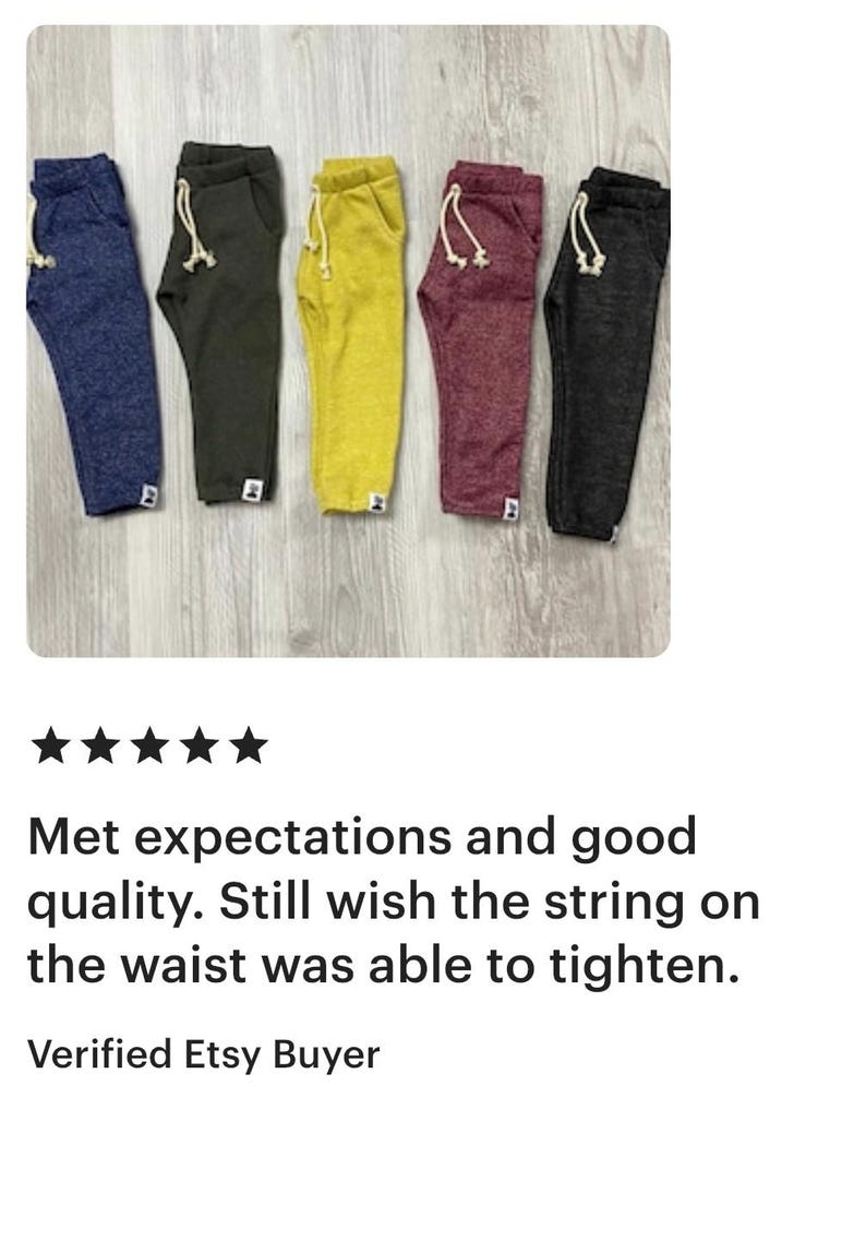 May include: Five pairs of sweatpants in navy blue, olive green, yellow, burgundy, and charcoal grey. Each pair has a drawstring waist and a small white tag. The pants are displayed on a light wood surface.